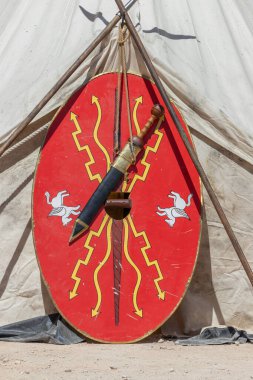 Dikey olarak, kırmızı renkli oval bir kalkan ve antik toman imparatorluğunun yedek birliklerinin kılıcı görünüyor.