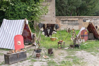 Antik Roma zamanından kalma bir askeri kampın yatay görüntüsü. Çadırlar, çatallar, giysiler, kalkanlar ve bir Roma lejyoner askerinin mızrakları.