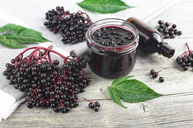Cam kavanozda nefis ev yapımı siyah mürver şurubu ve ahşap masa üzerinde yeşil yapraklı bir demet siyah mürver..