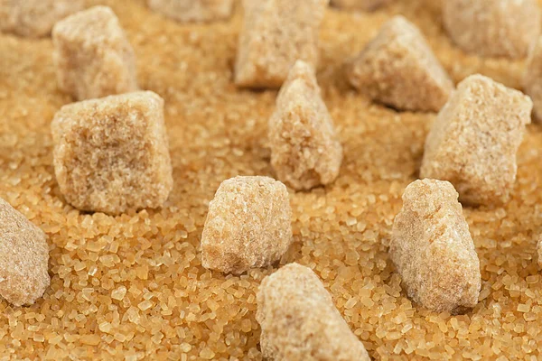 Brown sugar cubes on cane sugar crystals, close up. Demerara golden sugar.