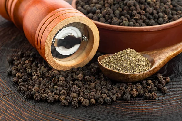 Wooden pepper mill, black peppercorns and ground black pepper on old wooden table.