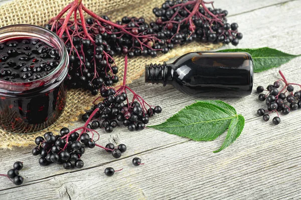 Black elderberry fruit on vintage wooden board, Sambucus. Branches of elderberry with green leaves, elderberry jam, syrup and confiture. European black elderberry. Alternative medicine and lifestyle.