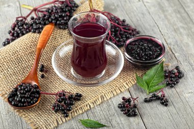 Elderberry şurubu içinde cam bir beher içinde bir demet mürver ve ahşap bir masa üzerinde yeşil mürver yaprakları. Alternatif tıp ve yaşam tarzı