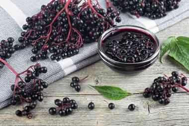 Taze olgun siyah mürver, mürver şurubu ve kırsal ahşap arka planda mürver yaprakları. Alternatif tıp ve yaşam tarzı.