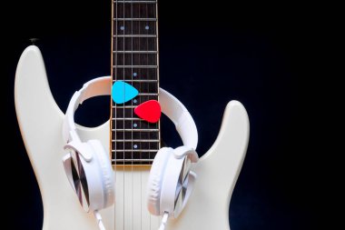 Beyaz elektro gitarda beyaz kulaklık, siyah arka planda mavi ve kırmızı penalar.