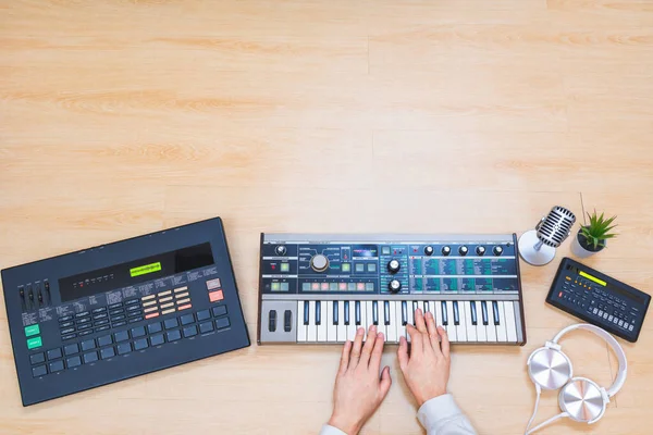 male musician hands playing synthesizer keyboard with drum machine, sequencer and headphone on wooden desk