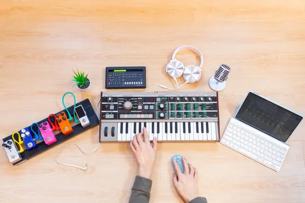 male musician hands playing keyboard synthesizer with tablet computer, sequencer, effect processor, headphone and microphone on wooden desk. music production concept
