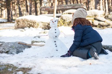 Kızıl saçlı kız, karlı ormanda kardan adamla oynuyor. Kış. Arkadan bak. Yatay çerçeve.