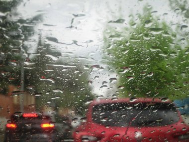 A tight shot of a rain-splattered window, revealing a traficc car background. Up-close view of raindrops on window clipart