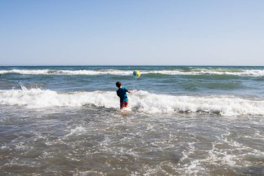 Kızıl saçlı erkek, kumsalda mavi t-sirt ile top oynuyor. Deniz. Yatay olarak. Boşluğu kopyala