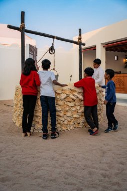 DOHA, Qatar - December 13, 2024: Children stand in front of an old water well at Darb Al Saai during the National Day celebrations. clipart