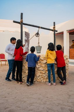 DOHA, Katar - 13 Aralık 2024: Ulusal Bayram kutlamaları sırasında Darb Al Saai 'deki eski bir su kuyusunun önünde duran çocuklar.