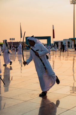 DOHA, Katar - 13 Aralık 2024: Beyaz bir Katar abayası içindeki bir adam Ulusal Bayram kutlamaları sırasında Darb Al Saai 'de kılıç dansı yapıyor.