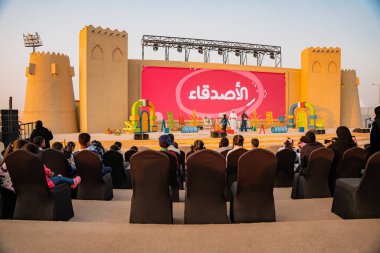 DOHA, Qatar - December 13, 2024: A group of children sit on a stage at Darb Al Saai during the National Day celebrations. clipart