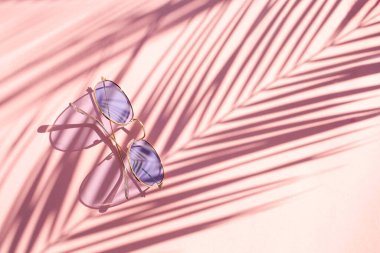 Pembe arka planda mavi güneş gözlüğü ve zıt palmiye yapraklarının gölgeleri. Düzleştirme biçimi