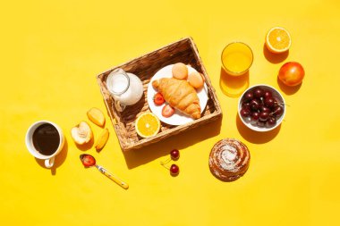 Sarı arka plan manzaralı bir fincan kahve, meyve ve kruvasanla kahvaltı. Düzleştirme biçimi