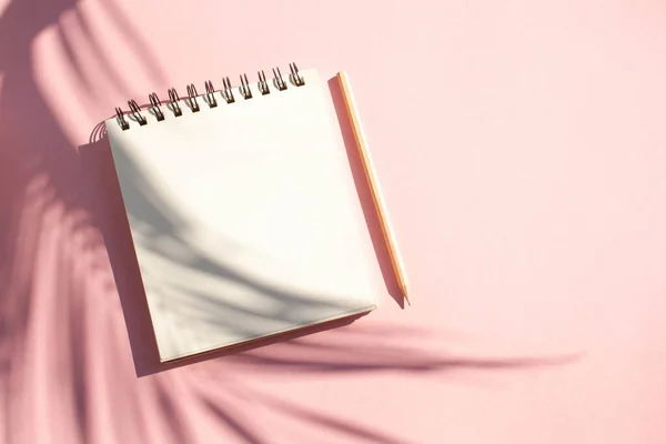 Kalemli ve pembe arka planda bir palmiye yaprağının zıt gölgesi olan defter. Düzleştirme biçimi