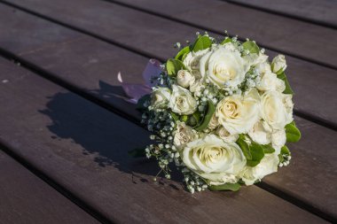 Güzel bir buket beyaz gül ve yeşillik ahşap bir yüzeye bir gölge düşürür, saflığı ve zarafeti sembolize eder.