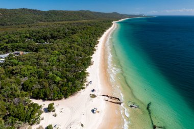 Moreton Adası, Queensland, Avustralya 'daki el değmemiş plajlarda gemi enkazı ve off-road araçları.