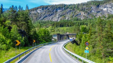 Norveç 'in güzel manzarası boyunca uzun ve boş bir yol. Etrafı yeşil dağ tepeleriyle çevrili. Gün ışığında açık mavi gökyüzü günü.