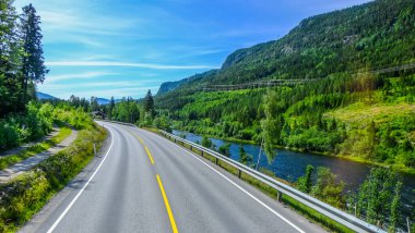 Norveç 'in güzel manzarası boyunca uzun ve boş bir yol. Etrafı yeşil dağ tepeleriyle çevrili. Gün ışığında açık mavi gökyüzü günü.