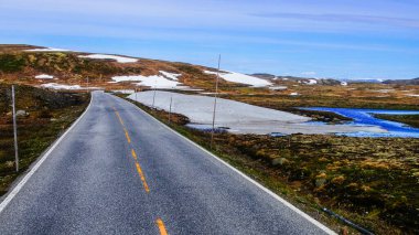 Kuzey Norveç 'in güzel manzarası boyunca uzanan yol kısmen karla kaplı dağ tepeleriyle çevrilidir.