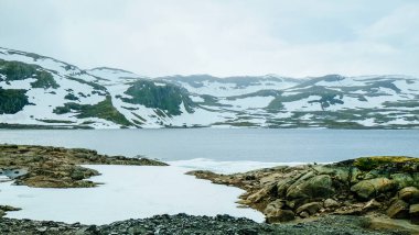 Norveç kırsalında buzla kaplı kar tepecikli dağ ve gölün kış manzarası