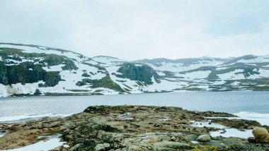 Norveç kırsalında buzla kaplı kar tepecikli dağ ve gölün kış manzarası