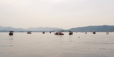 Çin 'in Hangzhou kentindeki sisli dağlarla çevrili Batı Gölü' nde turistlerin gezdiği geleneksel ahşap tekneler.
