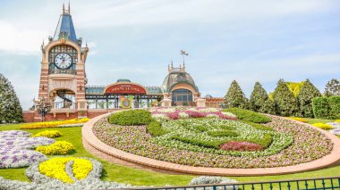 Shanghai Disneyland girişinde Minnie Mouse çiçek tarhı sergilenen renkli bir çiçek sergisi. Parkların ikonik saat kulesi ve turistleri karşılayan bir tabela.