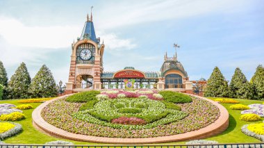 Shanghai Disneyland girişinde Minnie Mouse çiçek tarhı sergilenen renkli bir çiçek sergisi. Parkların ikonik saat kulesi ve turistleri karşılayan bir tabela.