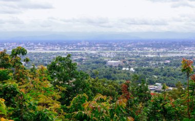 Tayland 'ın Chiang Mai şehrinin panoramik hava manzarası, bir dağ tarafından görülüyor. Dağlarla çevrili kentsel gelişimle yemyeşil bir arazi.