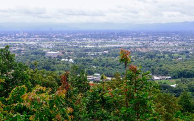 Tayland 'ın Chiang Mai şehrinin panoramik hava manzarası, bir dağ tarafından görülüyor. Dağlarla çevrili kentsel gelişimle yemyeşil bir arazi.