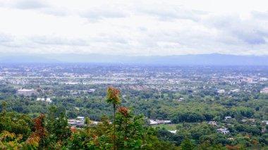 Tayland 'ın Chiang Mai şehrinin panoramik hava manzarası, bir dağ tarafından görülüyor. Dağlarla çevrili kentsel gelişimle yemyeşil bir arazi.