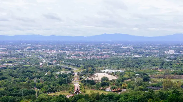 Tayland 'ın Chiang Mai şehrinin panoramik hava manzarası, bir dağ tarafından görülüyor. Dağlarla çevrili kentsel gelişimle yemyeşil bir arazi.