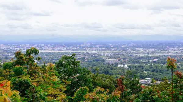 Tayland 'ın Chiang Mai şehrinin panoramik hava manzarası, bir dağ tarafından görülüyor. Dağlarla çevrili kentsel gelişimle yemyeşil bir arazi.