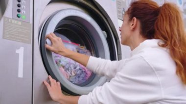 Ev hanımı genç kadın ev işi yapıyor, düzenli temizlik işleriyle meşgul çamaşır makinesine havlu koyuyor, rahat çamaşır odasındaki modern çamaşır makinesini açıyor. Ev işleri konsepti.