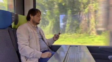 Trende oturan, rahatlayan ve akıllı telefon kullanan adam. Yaratıcı adam sosyal medyayı kontrol ediyor, arkadaşlarıyla sohbet ediyor, internette geziniyor. Yüksek kalite 4k görüntü