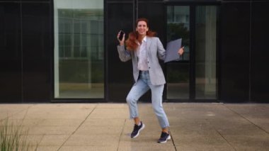 Genç beyaz iş kadını iş bölgesinde çalışırken müzikle dans ediyor. Çekici, güzel, resmi kıyafetli kadın çalışanlar müzik dinlemekten ve dans etmekten hoşlanırlar. Yüksek kalite 4k görüntü