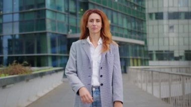 Çekici, kendine güvenen, gülümseyen, çeşitli kurumsal resmi bir kadın ofis binasının önünde duruyor ellerini katlıyor, kameraya bakıyor ve gülümsüyor. Yüksek kalite 4k görüntü