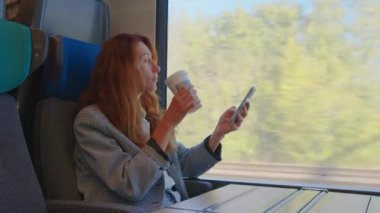 Trende oturan güzel bir kadın, dinleniyor ve akıllı telefon kullanıyor. Yaratıcı kız sosyal medyayı kontrol ediyor, arkadaşlarıyla sohbet ediyor, internette geziniyor. Yüksek kalite 4k görüntü