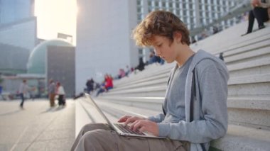 Yoğunlaşmış genç programcı dizüstü bilgisayara bakıyor, dışarıda çalışıyor. Kafa resmi odaklı gülümseyen adam sosyal ağda sohbet ediyor, mesaj yazıyor, internet sörfü yapıyor..