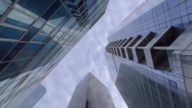 Cam gökdelenler mavi gökyüzünü bulutlarla yansıtıyor. Modern bir iş bölgesinde kamera hareketi. Başarılı iş konsepti. Yüksek kalite 4k görüntü