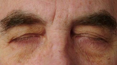 Yaşlı bir adama yakın planda kalın kaşlar. Yaşlı bir adamın yüzü ve gözleri. Yaşlı bir adamın yüzünde büyük kırışıklıklar var. Yüzünü yaklaştır. Yaşlı bir vatandaş kameraya bakar. Yüksek kalite 4k