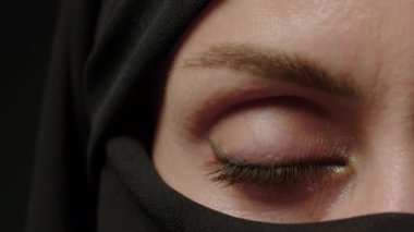 Close-up portrait of a Muslim woman with beautiful eyes in a hijab on a dark background. A girl in a black headscarf is looking at the camera. Arab women life concept. High quality 4k footage