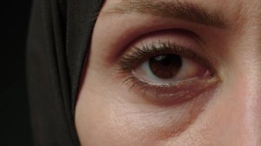 Close-up half-portrait of young muslim woman in hijab with fashionable make-up watching in camera on black background. High quality 4k footage