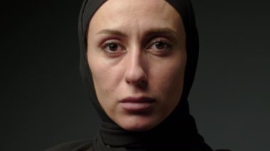 Close-up portrait of a Muslim woman with beautiful eyes in a hijab on a dark background. A girl in a black headscarf is looking at the camera. Arab women life concept. High quality 4k footage