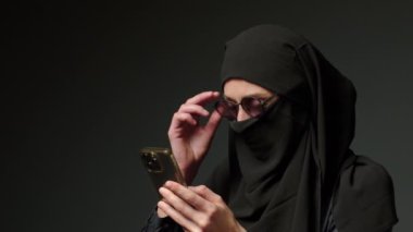 Woman in black muslim headscarf talking on mobile phone. Young arab muslim girl in headscarf hijab using smart phone, close up portrait of smiling middle eastern girl holding mobile smartphone.