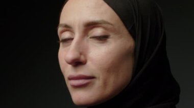Close-up portrait of a Muslim woman with beautiful eyes in a hijab on a dark background. A girl in a black headscarf is looking at the camera. Arab women life concept. High quality 4k footage