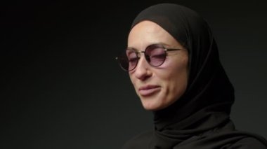 Portrait of beautiful young Arab muslim woman in black traditional hijab looking straight to camera and smiling. Close up of female pretty face with smile. Arabian headscarf. High quality 4k footage